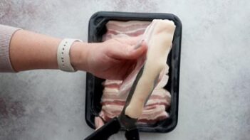 Cutting the pork skin off of pork belly with kitchen shears.