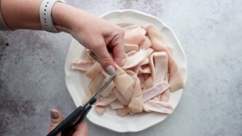 Cutting pork skin in half with scissors.