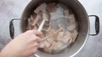 Stirring pork skins boiling in a large pot of water.