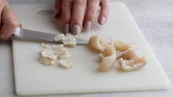 Using a paring knife to trim off the fat from pork skin pieces.