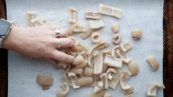 A hand scattering pork skins on a baking sheet lined with parchment paper.