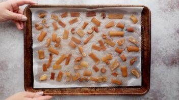 Two hands holding a baking tray with baked, dried pork skins on top.