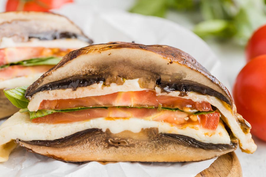 Close up of the layers of a Portobello mushroom sandwich with tomato, mozzarella and basil inside.
