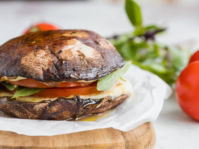 Portobello mushroom sandwich with tomato, cheese and greens on parchment paper.
