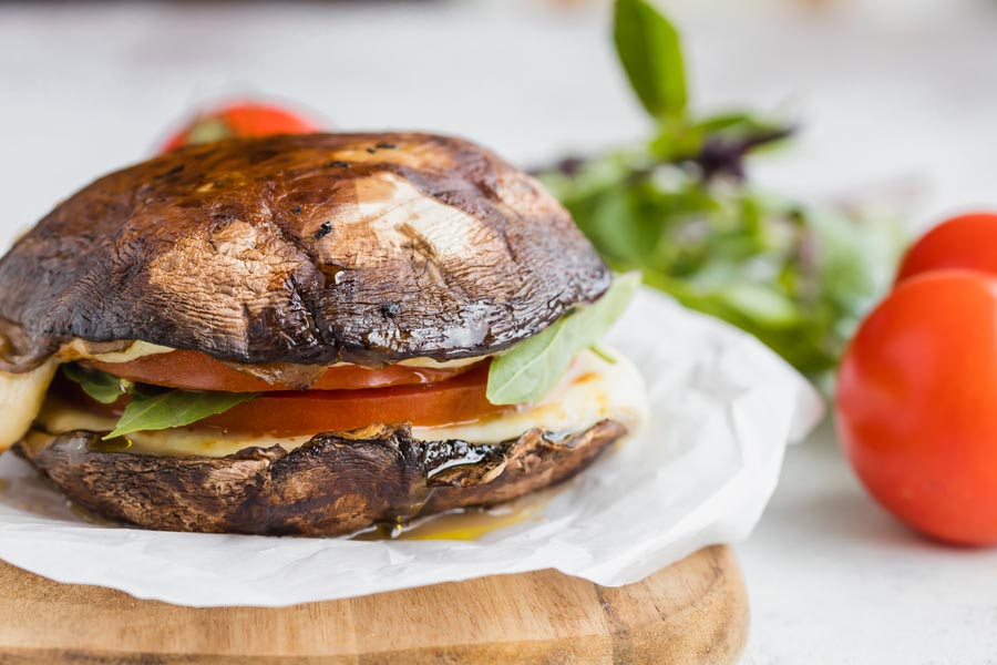 A mushroom cap sandwich made from Portobello mushrooms on a piece of parchment paper next to tomatoes.