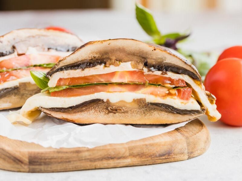 A half of a mushroom sandwich filled with melted cheese, sliced tomato and basil.