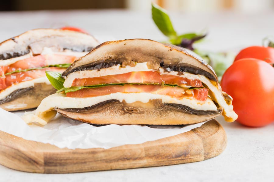 A half of a mushroom sandwich filled with melted cheese, sliced tomato and basil.