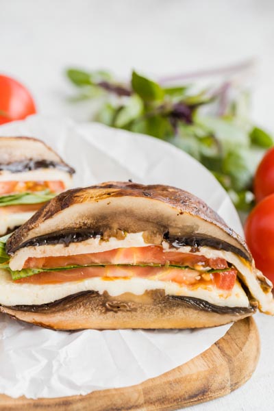 A mushroom sandwich cut in half filled with Italian ingredients like mozzarella cheese, tomato and basil.