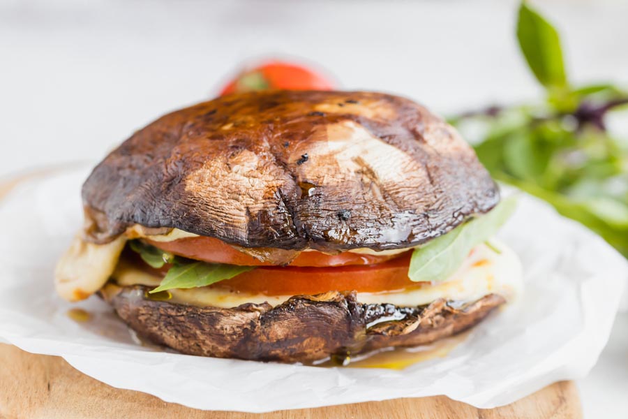 A sandwich with mushroom caps for bread sits on a piece of parchment paper.