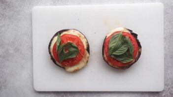 Two mushrooms topped with melted cheese, sliced tomato and fresh basil.