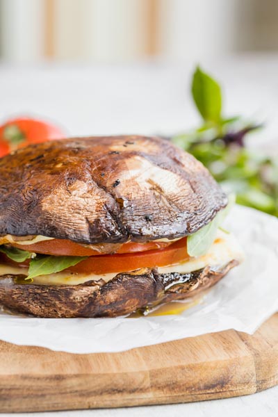 A mushroom cap sandwich on a cutting board filled with tomato and cheese.