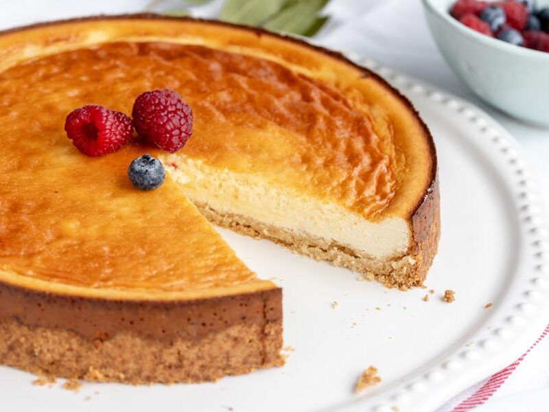 A slice missing from a whole New York cheesecake topped with three berries.
