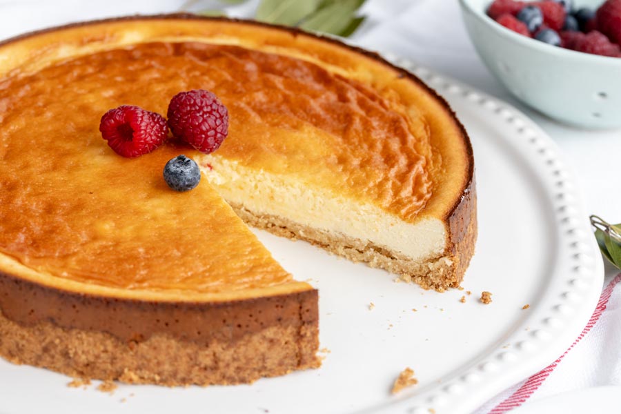 A slice missing from a whole New York cheesecake topped with three berries.