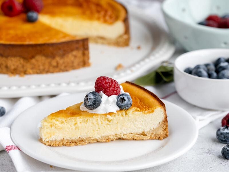 Slice of protein cheesecake topped with whipped cream, raspberries and blueberries.