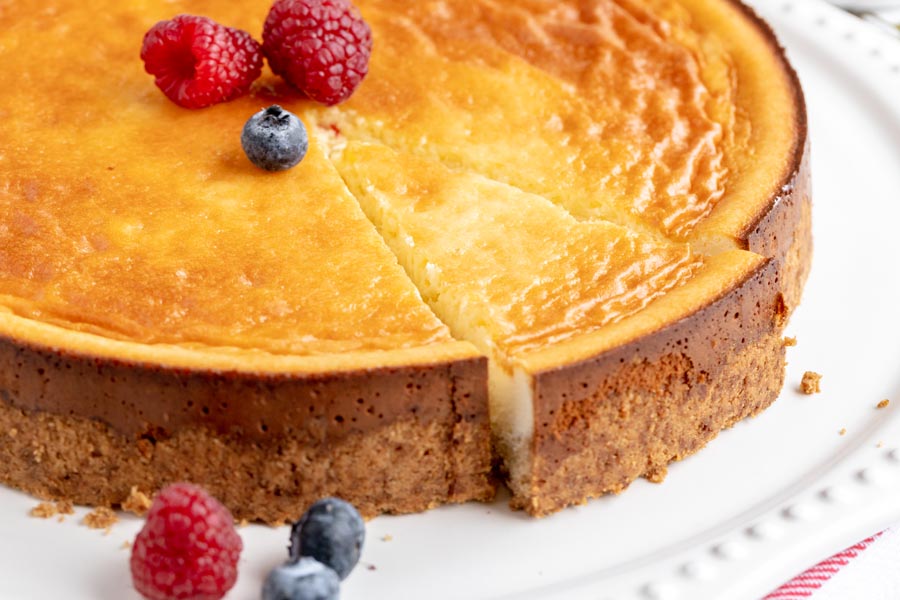 A slice of cheesecake cut out of a whole cake. The slice is slightly pushed out. Fresh berries are nearby.