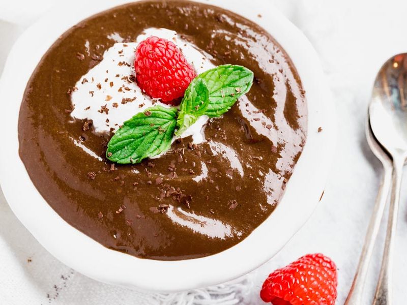 creamy, thick chocolate pudding with raspberries, whipped cream and mint next to two spoons