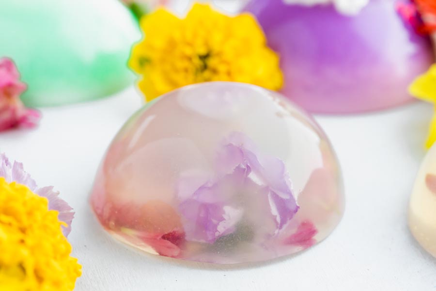 A mini dome shaped cake that looks like a droplette of water with flowers inside. Yellow flowers surround the cake.