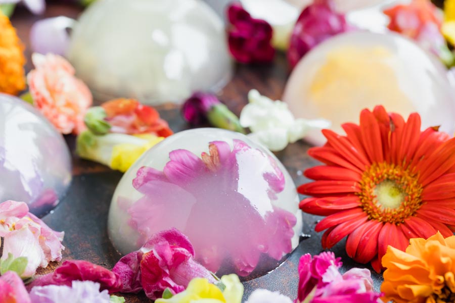 Clear raindrop cakes next to a bunch of colorful edible flowers.