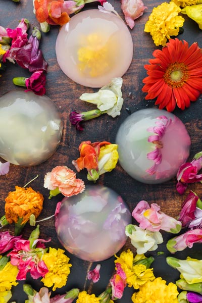 Four clear raindrop cakes filled with edible flowers surrounding flowers.