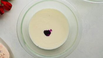 A bowl with cream and a few drops of purple food coloring inside.