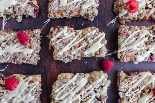 a bunch of white chocolate covered granola bars lined up with raspberries scattered around