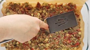 pressing granola bars into a baking pan with a spatula