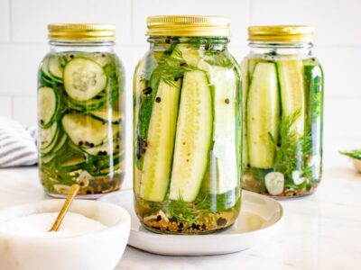 Three jars of homemade refrigerator pickles filled with cucumber slices and spears, fresh dill, garlic, and pickling spices in a vinegar brine.