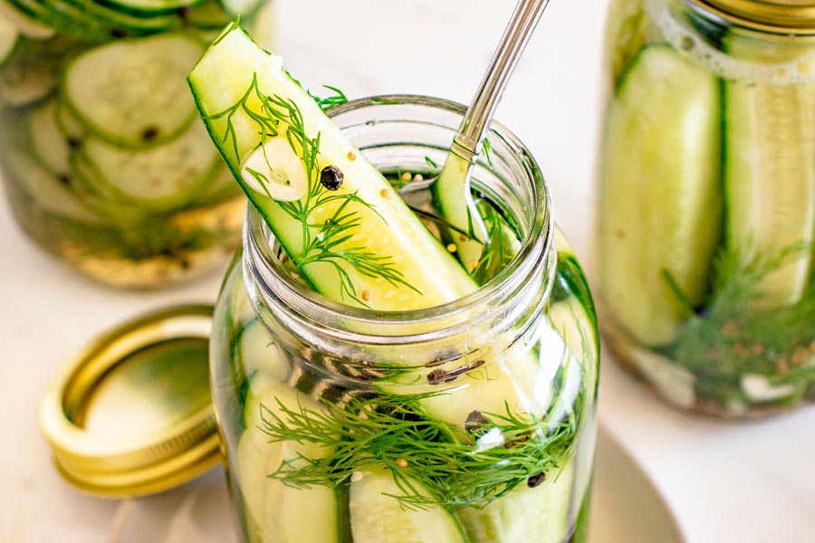 A crisp refrigerator dill pickle spear lifted from a jar of homemade pickles with fresh dill, garlic, and pickling spices.