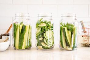 Three mason jars filled with fresh cucumber slices and spears, garlic, and dill before adding the pickling brine.