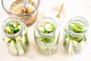 Overhead view of three mason jars packed with cucumbers, fresh dill, and garlic, ready for homemade refrigerator pickling brine.