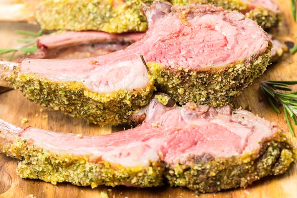 two lamb ribs sliced with a mustard herb crust on a cutting board