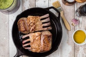 pan seared rack of lamb in a cast iron skillet with a brush nearby