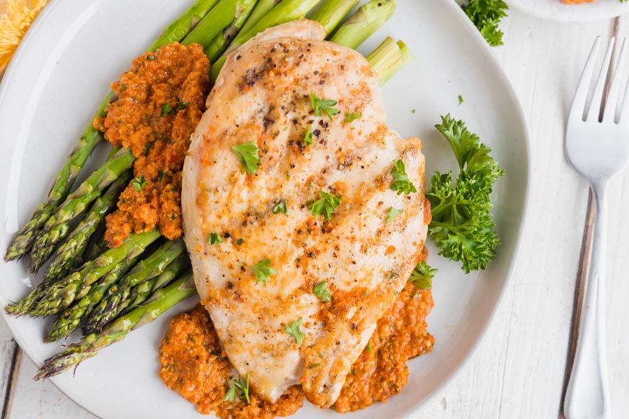 grilled chicken topped with romesco and aspargus on a plate with parsley