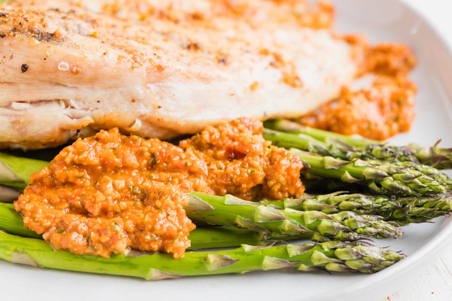 red, creamy romesco sauce on top of roasted asparagus