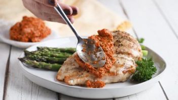 pouring romesco sauce on grilled chicken