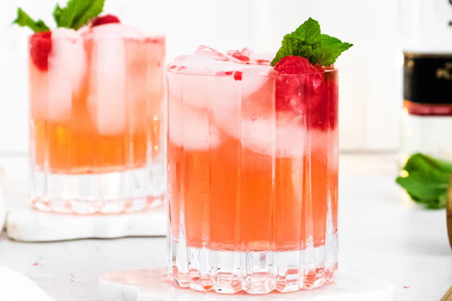 two chilled glasses of rose cocktail with ice, mint and raspberries
