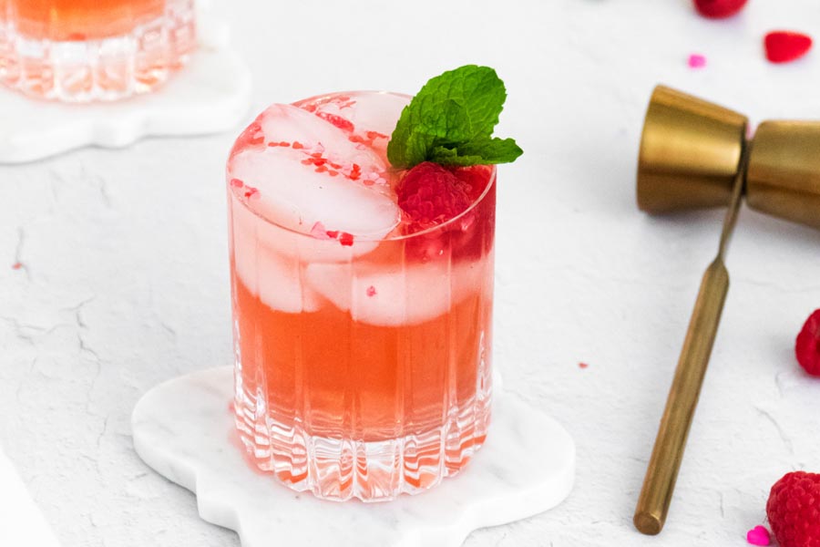 refreshing pinkish cocktail next to a jigger and raspberries