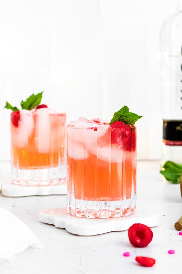 two cocktails in glasses topped with raspberries