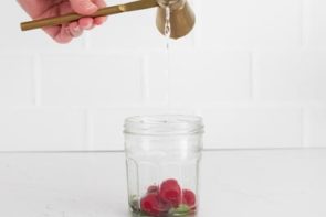 pouring vodka in a jar with raspberries in it