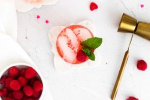 a red drink with mint leaves and a shot measurer next to it