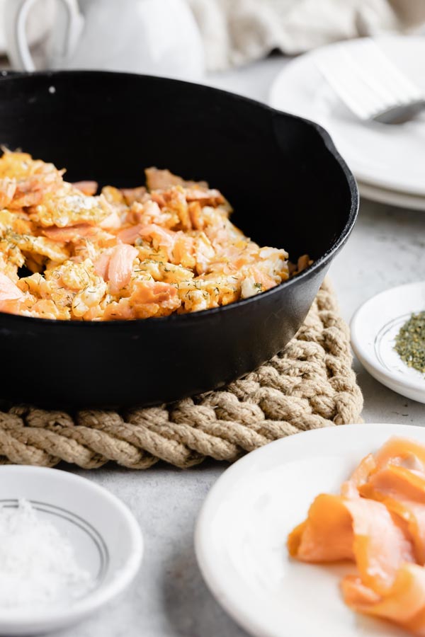 a skillet with scrambled eggs next to small plates with smoked salmon and salt near by