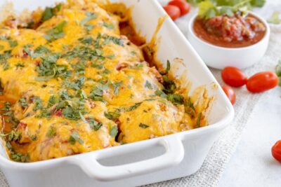 a white casserole dish with cheesy salsa chicken topped with cilantro next to a bowl of salsa