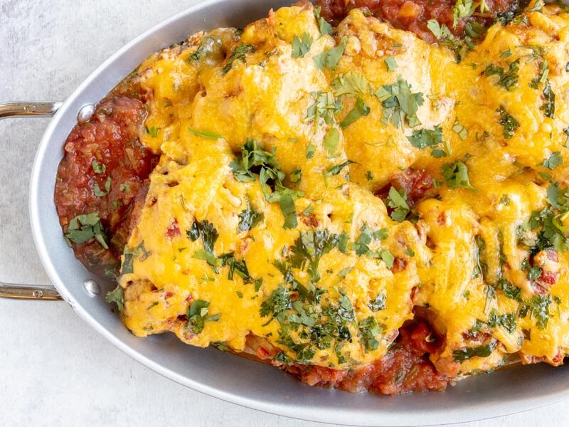 a skillet with baked salsa chicken topped with cheddar cheese and chopped cilantro