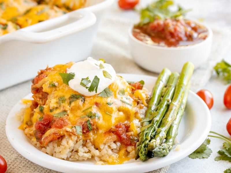 a plate with a serving of chicken salsa and cheese over cauliflower rice next to asparagus spears