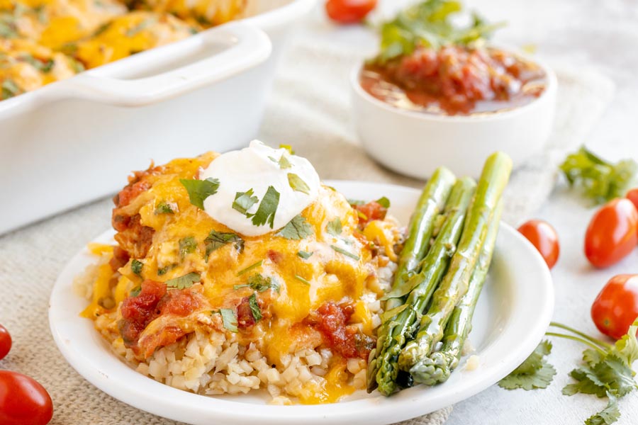 a plate with a serving of chicken salsa and cheese over cauliflower rice next to asparagus spears