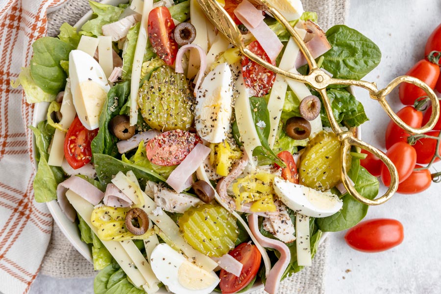 sandwich salad topped with black pepper and Italian seasoning and a pair of tongs