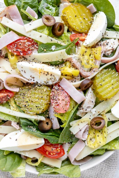 close up of a salad topped with pickle, olive, egg, ham, tomato