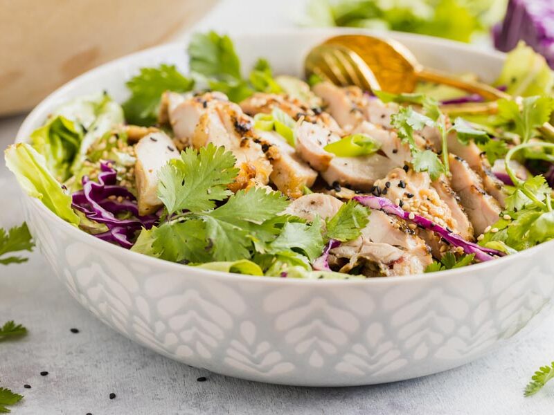 a sage green salad bowl filled with a chicken salad and topped with black and toasted sesame seeds