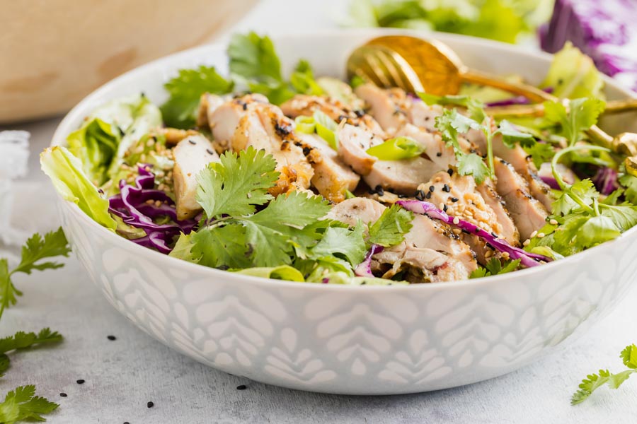 a sage green salad bowl filled with a chicken salad and topped with black and toasted sesame seeds