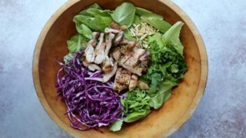 lettuce, chicken and red cabbage sit in a large wooden bowl